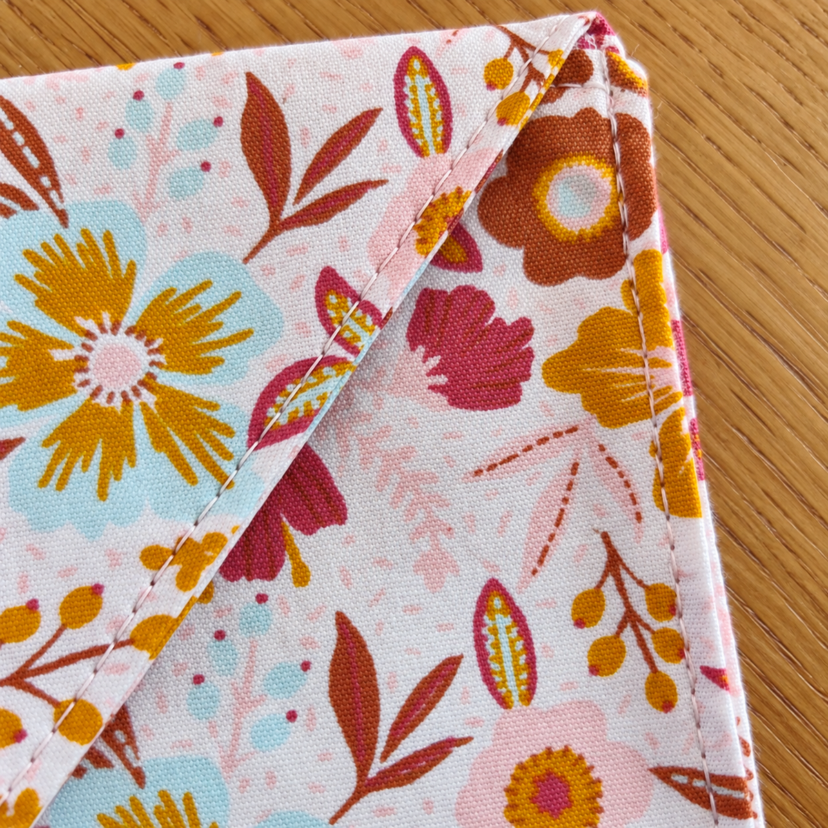 Close-up van een stoffen cadeauenvelop met kleurrijke bloemenprint en doorstiksel langs de rand.