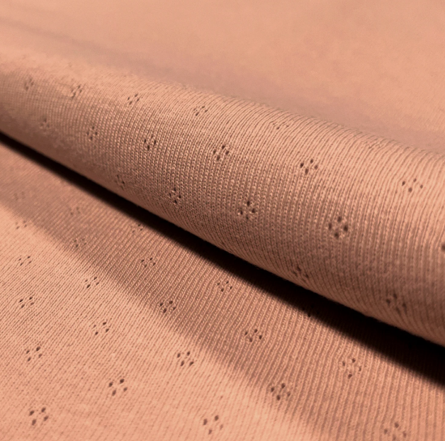 Close-up van koraalkleurige ajourstof met subtiel ruitmotief – Atelier KVG