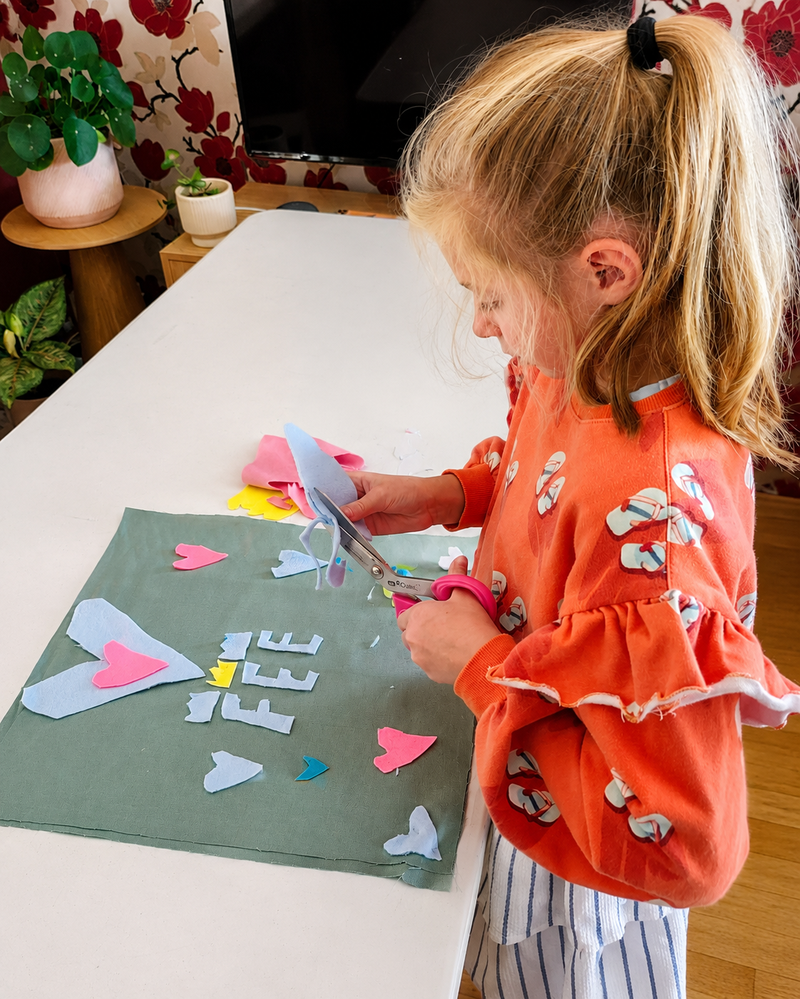 Kind knipt kleurrijke vilten vormen om een zelfgemaakte totebag te personaliseren