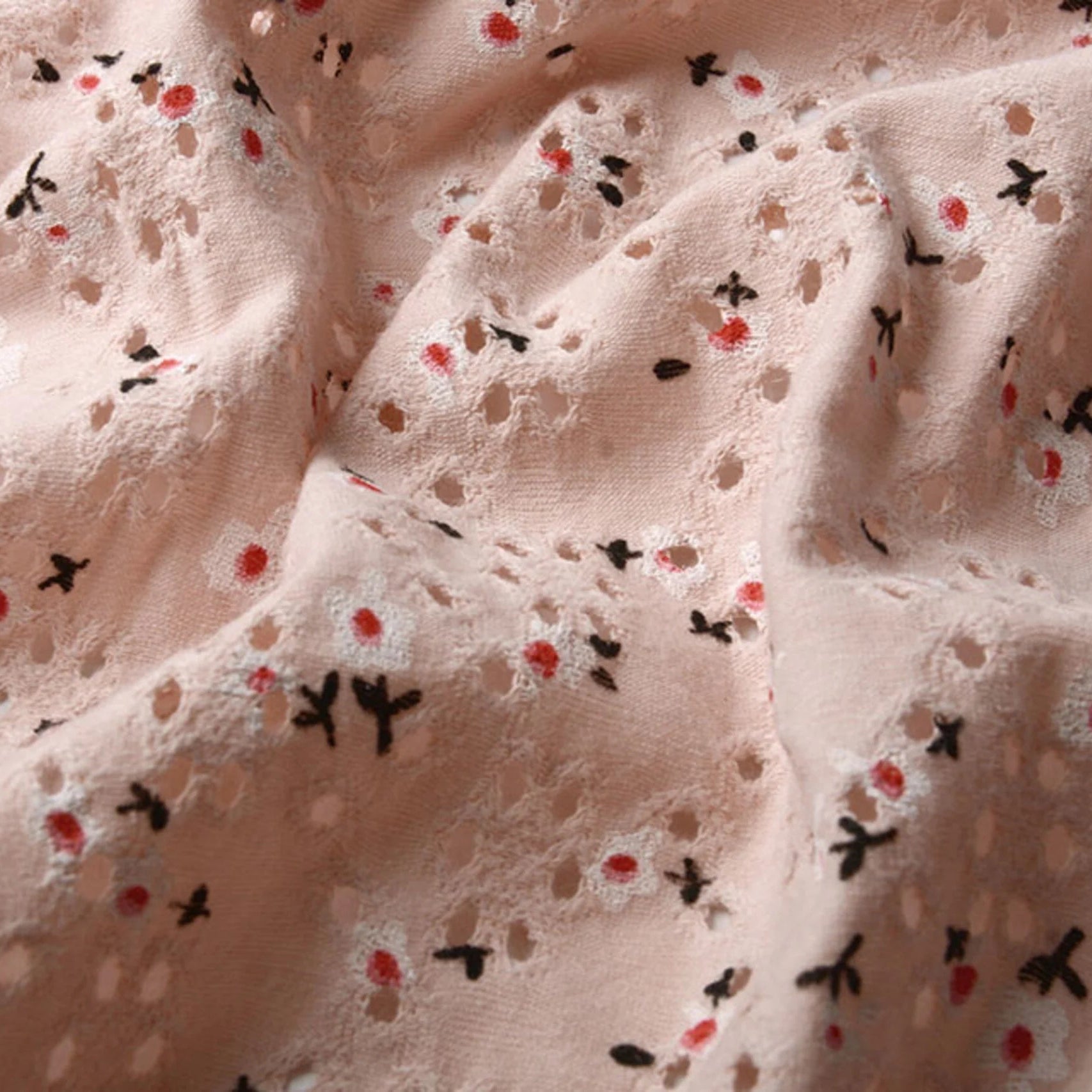 Close-up van opengewerkte poederroze broderie jersey met bloemenprint